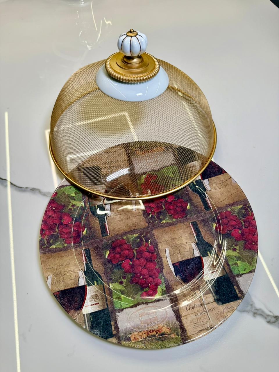 Elegante e funcional, o Suporte Gourmet Real é perfeito para servir e proteger alimentos com charme. Com base sofisticada e cúpula em tela metálica dourada, ele mantém os pratos protegidos enquanto valoriza a mesa posta. Ideal para queijos, bolos, pães e petiscos, trazendo um toque clássico e refinado para qualquer ocasião.